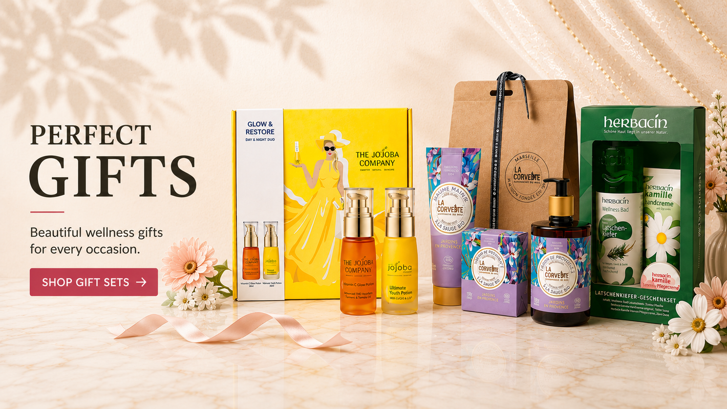 Premium gift sets including The Jojoba Company, La Corvette and Herbacin beautifully arranged with flowers on a luxury marble background.